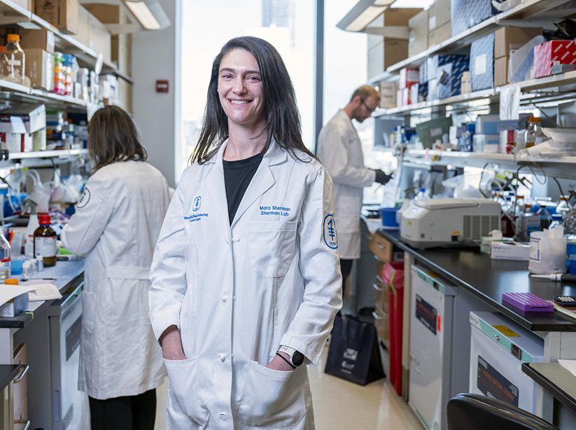 MSK cancer biologist Dr. Mara Sherman in an MSK lab. Two researchers standing in front of workbenches are in the background.