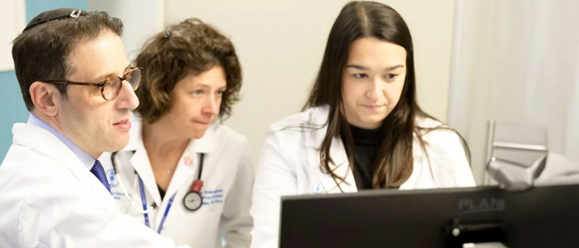 Three MSK blood cancer specialists look at a computer monitor.  