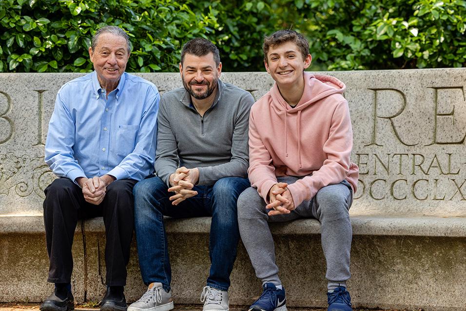 MSK patients Lenny, Judah, and Michael Deutsch sit together on a marble bench with greenery behind them.