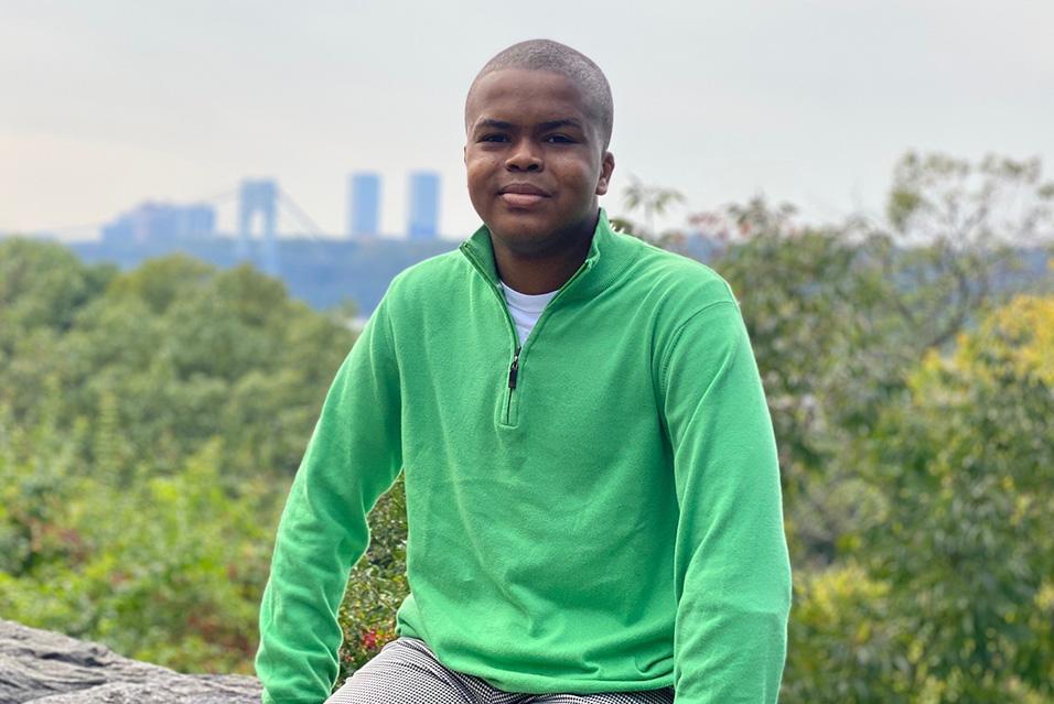 Mo Campbell, who was an MSK pediatric patient, sits outdoors with trees and a city skyline behind him.
